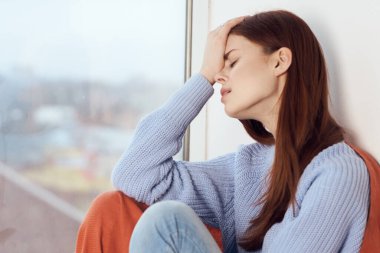 Hüzünlü yüzü olan kadın elinde ekoseyle pencerenin kenarında oturuyor.