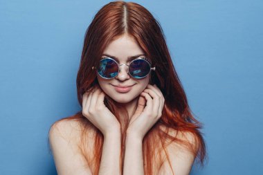 Çıplak omuzlu, gözlüklü, mavi arka planlı çekici bir kadın.