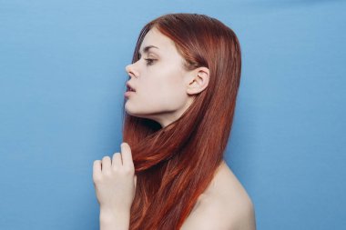 Çıplak omuzlu çekici bir kadın. Kızıl, yakın plan, mavi arka plan.