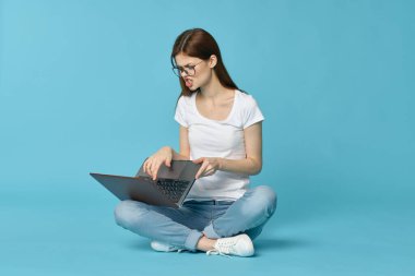 Dizüstü bilgisayarı olan kadın yerde oturuyor ve mavi arka planda öğrenci teknolojisi öğreniyor.