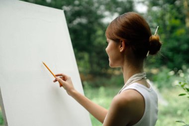 Doğada bir sanatçı kalemle sehpaya resim çizer.