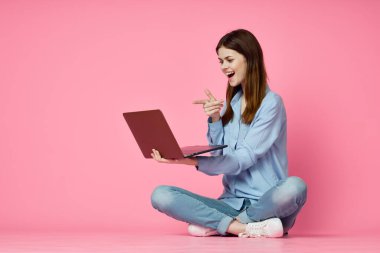 Dizüstü bilgisayar alışverişi yapan pembe arka planda oturan bir kadın.