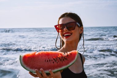 Ellerinde karpuz olan siyah mayo giymiş güzel bir kadın.