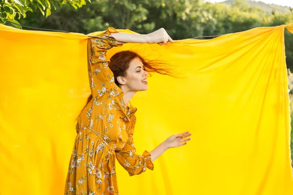 Sarı elbiseli gülümseyen kadın doğaya sarılık pozu veriyor.