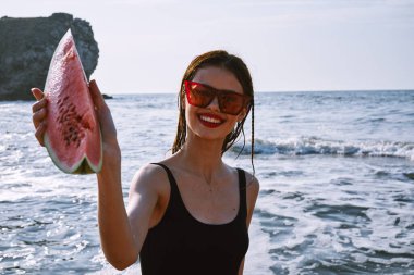 Ellerinde karpuz olan siyah mayo giymiş güzel bir kadın.