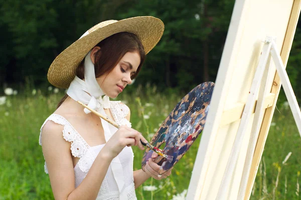 Bonita mujer en sombrero artista pinta un cuadro en la pintura de la naturaleza — Foto de Stock