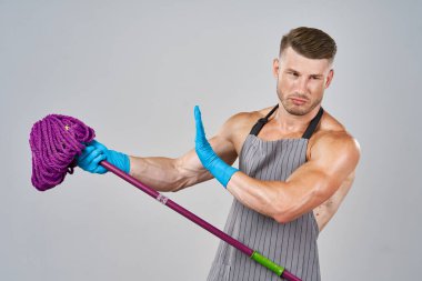 Elinde paspasla ev işi yapan önlüklü bir adam.