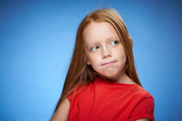 Carino dai capelli rossi ragazza in rosso t-shirt emozioni sfondo blu — Foto Stock