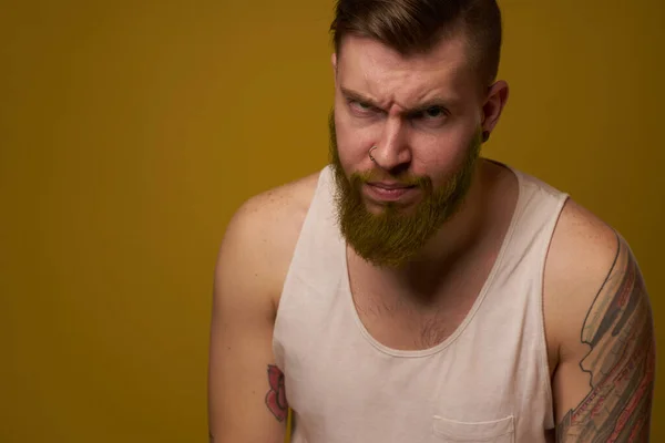 Бородатый мужчина с серьезным лицом в белой футболке с татуировками на руках — стоковое фото