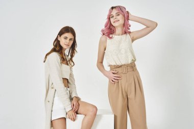 İki kız arkadaş yan yana durur. Moda cazibesi pozu verir.