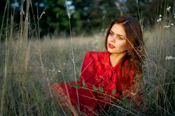 Femme dans une robe rouge se trouve sur l'herbe dans le domaine nature mode — Photo