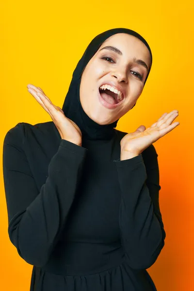 Muzułmanin w czarny hidżab pozowanie moda ręka gest żółty tło — Zdjęcie stockowe