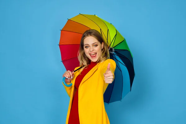 Vrouw in gele jas veelkleurige paraplu poseren blauwe achtergrond — Stockfoto