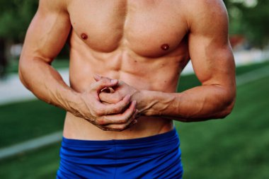 Şişirilmiş kaslı vücutlu bir adam dışarıda sağlık egzersizi yapıyor.