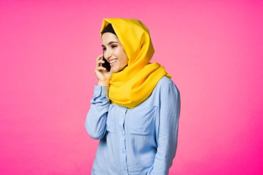 Sarı tesettürlü müslüman kadın telefon teknolojisi pembe arka planda konuşuyor.