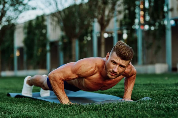 athletic man with pumped up muscular body in the park doing exercise