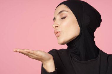neşeli Müslüman kadın siyah tesettüre poz veren el hareketi pembe arka plan