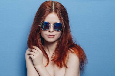 Şık kızıl saçlı, mavi gözlüklü, çıplak omuzlu bir kadın.