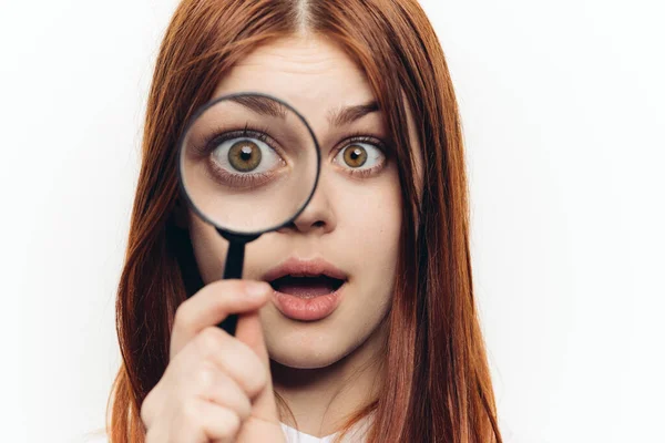 Femme aux cheveux roux dans une chemise blanche avec une loupe dans ses mains à la recherche — Photo