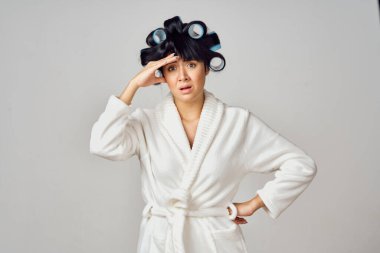 Kafasında bigudileri olan beyaz cüppeli bir kadın mutfakta ödev yapıyor.