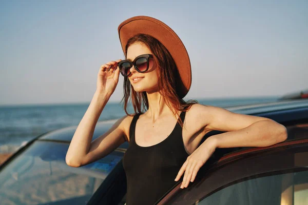 Fröhliche Frau mit Sonnenbrille und Hut auf dem Meer in der Nähe des Autos — Stockfoto