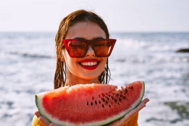 Okyanus kıyısındaki sahilde karpuz yiyen bir kadın.