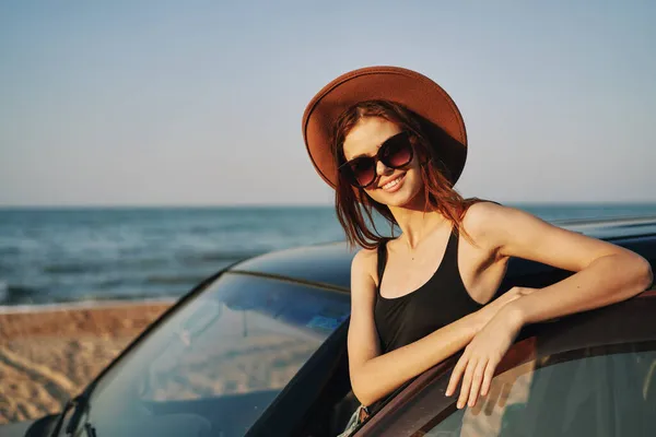 Fröhliche Frau mit Sonnenbrille und Hut auf dem Meer in der Nähe des Autos — Stockfoto