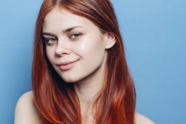 Çıplak omuzlu çekici bir kadın. Kızıl, yakın plan, mavi arka plan.