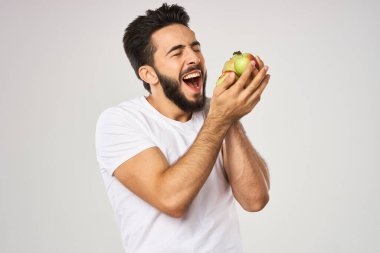 Beyaz tişörtlü sakallı bir adam sağlıklı yiyecekler tutuyor.