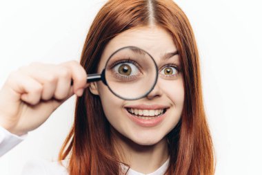 Ellerinde büyüteçle beyaz gömlekli kızıl saçlı bir kadın...