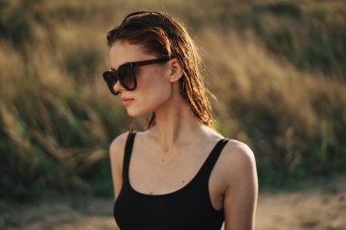 Güneş gözlüklü kadın doğada cips yiyor.