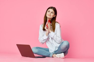 Pembe arka planda dizüstü bilgisayarı olan neşeli bir kadın.