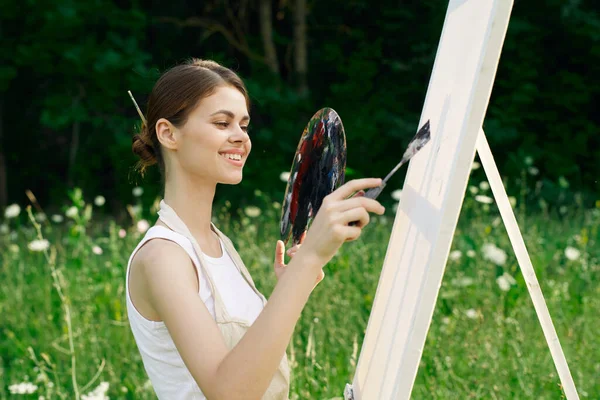 Mulher alegre pinta uma paleta de imagens paisagem natureza — Fotografia de Stock