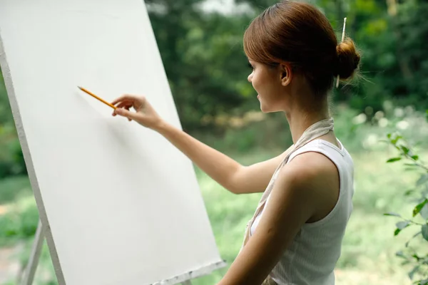 An artist in nature draws on an easel with a pencil — Stock Photo, Image