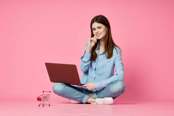 Mujer con el ordenador portátil sentado en la tecnología de piso de internet de compras fondo rosa — Foto de Stock
