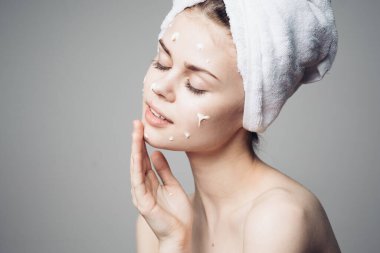 Çıplak omuzlu kadın yüz kremi sürmüş.