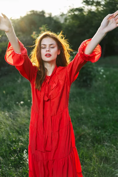 緑の草の中でポーズをとる赤いドレスの魅力的な女性 — ストック写真