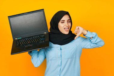 Elinde dizüstü bilgisayarla siyah tesettürlü kadın. Duyguları sarı arka planda.