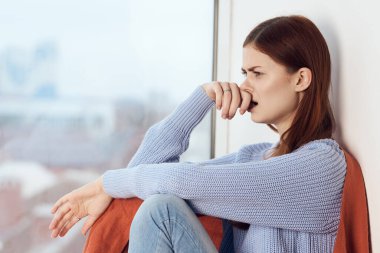 Hüzünlü yüzü olan kadın elinde ekoseyle pencerenin kenarında oturuyor.