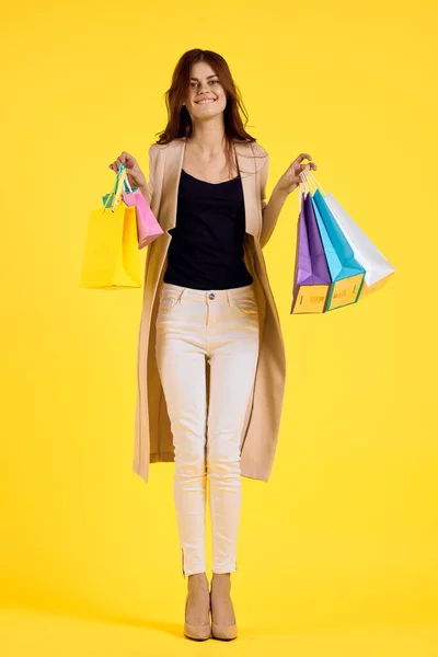 Mooie vrouw met veelkleurige tassen poseren gele achtergrond — Stockfoto
