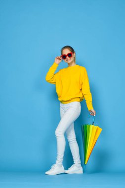 Sarı kazaklı, renkli şemsiyeli kadın gökkuşağı rengi pozlar veriyor.