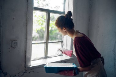 Kadın ressam fırça yenileme iç dekorasyonuyla pencereyi boyuyor.