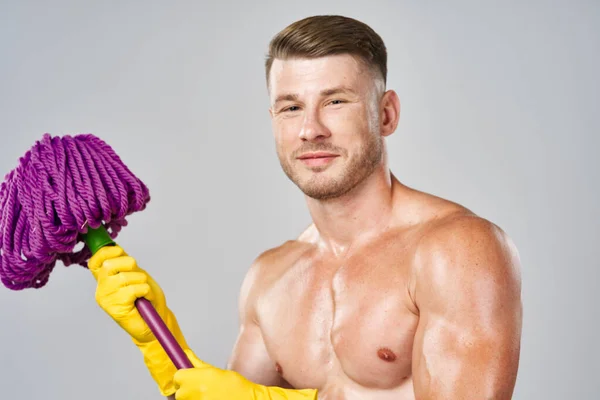 Ein Mann in gelben Handschuhen mit einem nackten Oberkörper und einem Wischmopp in den Händen — Stockfoto