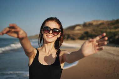 Siyah mayo giymiş neşeli bir kadın yaz mevsiminde sahilde yürüyor.