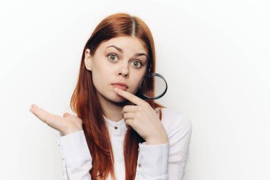 Neşeli kızıl saçlı kadın yüzünün yanında büyüteç tutuyor.