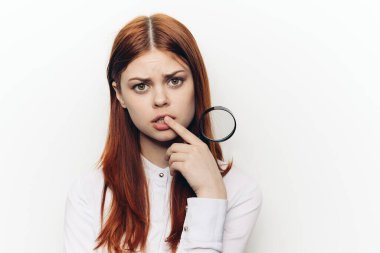 Neşeli kızıl saçlı kadın yüzünün yanında büyüteç tutuyor.