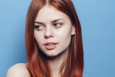 Çıplak omuzlu çekici bir kadın. Kızıl, yakın plan, mavi arka plan.