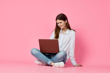 Yerde dizüstü bilgisayarlı bir kadın alışveriş teknolojisi pembe arka plan