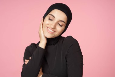 neşeli Müslüman kadın siyah tesettüre poz veren el hareketi pembe arka plan