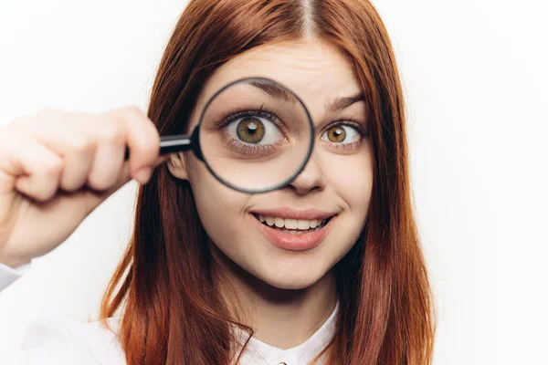 Mujer pelirroja con una camisa blanca con una lupa en las manos buscando — Foto de Stock